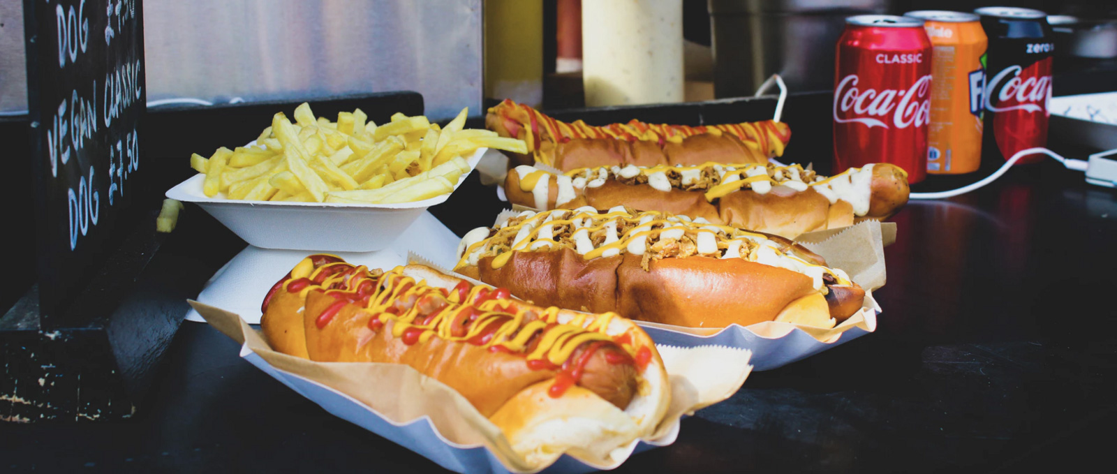 Several hot dogs and soda cans at an event 